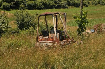 Poster - Rural landscape with a rusty old tractor in field the background of sown field and green forest