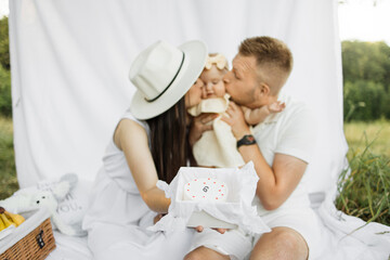 Wall Mural - Focus on delicious cake. Beautiful married couple with closed eyes kissing their six months old daughter with his birthday cake. Celebration, family and happiness concept.