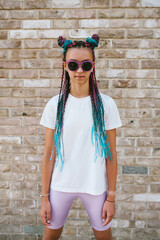 portrait of a cute teenage girl with african braids in a white t-shirt and sunglasses stands on a ci