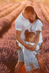 Wall Mural - happy family day. young father, mother and child daughter are hugging in the lavender field in sunset light. happy couple with kid enjoy summer holiday vacation. family look