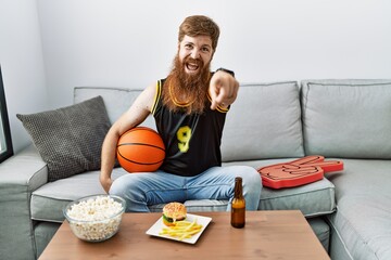 Poster - Caucasian man with long beard holding basketball ball cheering tv game pointing to you and the camera with fingers, smiling positive and cheerful