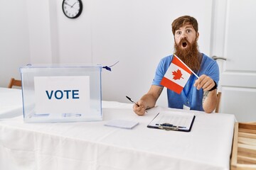 Canvas Print - Caucasian man with long beard at political campaign election holding canada flag scared and amazed with open mouth for surprise, disbelief face