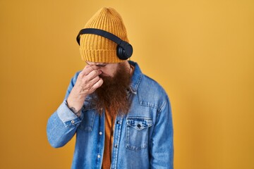 Poster - Caucasian man with long beard listening to music using headphones tired rubbing nose and eyes feeling fatigue and headache. stress and frustration concept.