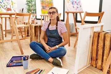 Wall Mural - Young brunette woman at art studio sitting on the floor puffing cheeks with funny face. mouth inflated with air, crazy expression.