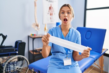 Poster - Young blonde woman holding therapy strip band afraid and shocked with surprise and amazed expression, fear and excited face.