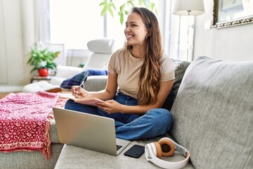 Young hispanic girl having online class sitting on the sofa at home.