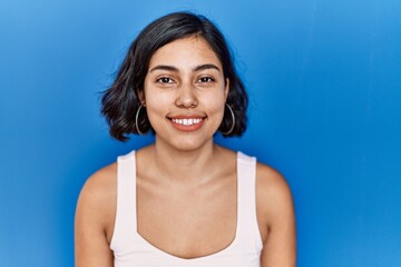 Wall Mural - Young hispanic woman standing over blue background with a happy and cool smile on face. lucky person.