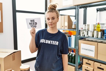 Poster - Young caucasian woman volunteer holding we need you banner thinking attitude and sober expression looking self confident