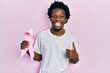 © Krakenimages.com - Young african american man holding pink cancer ribbon smiling happy and positive, thumb up doing excellent and approval sign