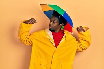 Poster - Young african american man wearing yellow raincoat showing arms muscles smiling proud. fitness concept.