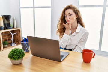 Poster - Young caucasian woman working at the office using computer laptop looking at the camera blowing a kiss with hand on air being lovely and sexy. love expression.