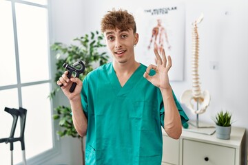 Sticker - Young caucasian physio man holding hand grip to train muscle at the clinic doing ok sign with fingers, smiling friendly gesturing excellent symbol