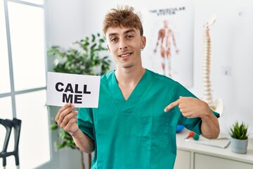 Sticker - Young caucasian physio man holding call me banner at the clinic pointing finger to one self smiling happy and proud