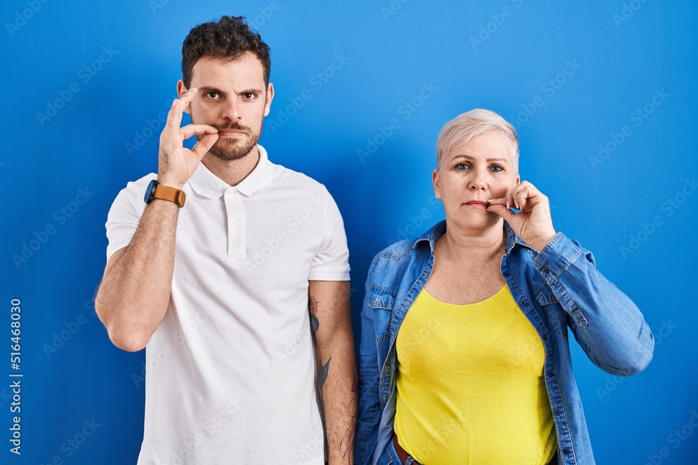 Young brazilian mother and son standing over blue background mouth and