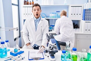 Poster - Hispanic man and woman working at scientist laboratory scared and amazed with open mouth for surprise, disbelief face