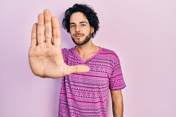 Sticker - Handsome hispanic man wearing casual pink t shirt doing stop sing with palm of the hand. warning expression with negative and serious gesture on the face.