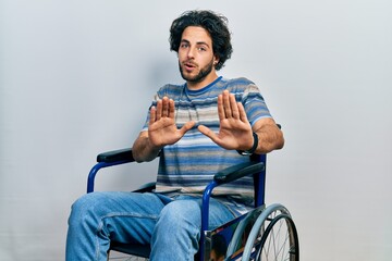 Wall Mural - Handsome hispanic man sitting on wheelchair moving away hands palms showing refusal and denial with afraid and disgusting expression. stop and forbidden.