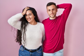 Sticker - Young hispanic couple standing over pink background smiling confident touching hair with hand up gesture, posing attractive and fashionable