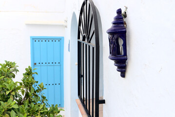 Closeup of old blue lantern of ceramic. Bars on window, green leaves plant and light blue door of wood in background. High quality photo