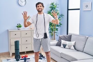 Wall Mural - Handsome latin man wearing sportswear at home showing and pointing up with fingers number nine while smiling confident and happy.