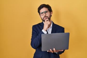 Canvas Print - Handsome latin man working using computer laptop looking confident at the camera smiling with crossed arms and hand raised on chin. thinking positive.