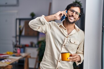 Sticker - Young hispanic man artist talking on the smartphone drinking coffee at art studio