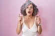© Krakenimages.com - Middle age woman with grey hair standing over pink background amazed and surprised looking up and pointing with fingers and raised arms.
