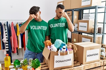 Canvas Print - Young gay couple wearing volunteer t shirt at donations stand tired rubbing nose and eyes feeling fatigue and headache. stress and frustration concept.