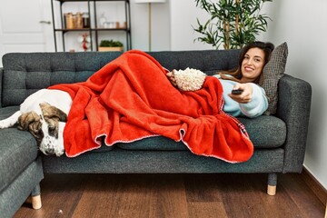 Young woman watching movie lying on sofa with dog at home