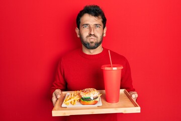 Sticker - Handsome man with beard eating a tasty classic burger with fries and soda puffing cheeks with funny face. mouth inflated with air, catching air.