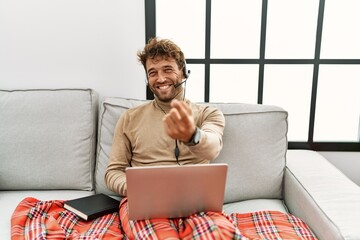 Poster - Young handsome man with beard wearing operator headset working from home beckoning come here gesture with hand inviting welcoming happy and smiling