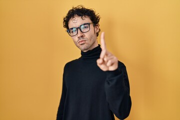 Sticker - Hispanic man standing over yellow background pointing with finger up and angry expression, showing no gesture