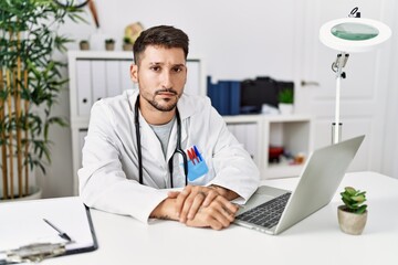 Poster - Young doctor working at the clinic using computer laptop skeptic and nervous, frowning upset because of problem. negative person.