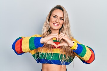 Sticker - Beautiful young blonde woman wearing colored sweater smiling in love doing heart symbol shape with hands. romantic concept.