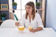 © Krakenimages.com - Young hispanic woman drinking glass of orange juice skeptic and nervous, frowning upset because of problem. negative person.
