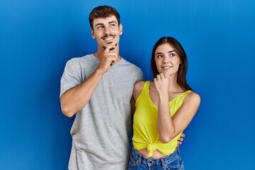 Poster - Young hispanic couple standing together over blue background with hand on chin thinking about question, pensive expression. smiling and thoughtful face. doubt concept.