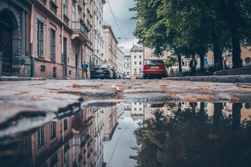 Rainy day in the big city, the cars drive along the old road. Close up view of a hatch at the level of the asphalt