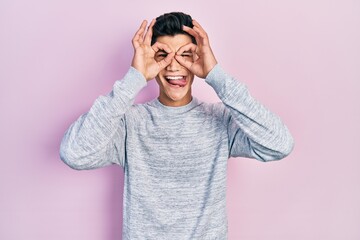 Sticker - Young hispanic man wearing casual clothes doing ok gesture like binoculars sticking tongue out, eyes looking through fingers. crazy expression.