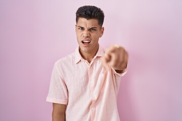 Wall Mural - Young hispanic man standing over pink background pointing displeased and frustrated to the camera, angry and furious with you