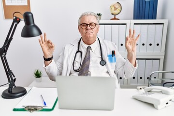 Wall Mural - Senior caucasian man wearing doctor uniform and stethoscope at the clinic relaxed and smiling with eyes closed doing meditation gesture with fingers. yoga concept.