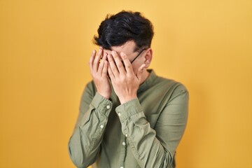 Poster - Non binary person standing over yellow background with sad expression covering face with hands while crying. depression concept.