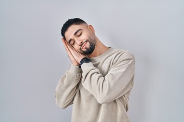 Canvas Print - Young handsome man standing over isolated background sleeping tired dreaming and posing with hands together while smiling with closed eyes.