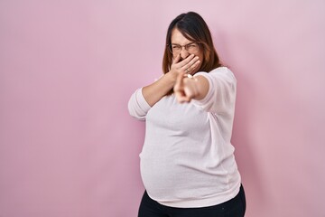 Poster - Pregnant woman standing over pink background laughing at you, pointing finger to the camera with hand over mouth, shame expression