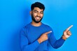 © Krakenimages.com - Arab man with beard wearing casual blue sweater smiling and looking at the camera pointing with two hands and fingers to the side.