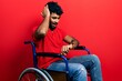 Arab man with beard sitting on wheelchair looking at the watch time worried, afraid of getting late