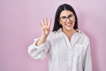 Sticker - Young brunette woman standing over pink background showing and pointing up with fingers number four while smiling confident and happy.