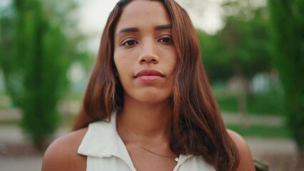 Wall Mural - Clouse-up, beautiful girl with brown long hair, tanned skin wearing white top raises her head and looks straight into the camera. Young women serious look at camera open and confident