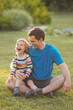 © Evgeniya Grande - Father and son playing and laughing together, sitting on grass in green park on summer day. Happy family concept