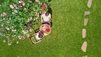 Young couple enjoying food and drinks in beautiful roses garden on romantic date, aerial top view from above of man and woman eating and drinking together outdoors in park
