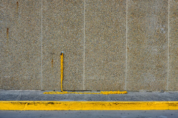 A pebblecrete concrete wall behind a gutter painted yellow, with a yellow polebollard, and yellow chain attached with a padlock.